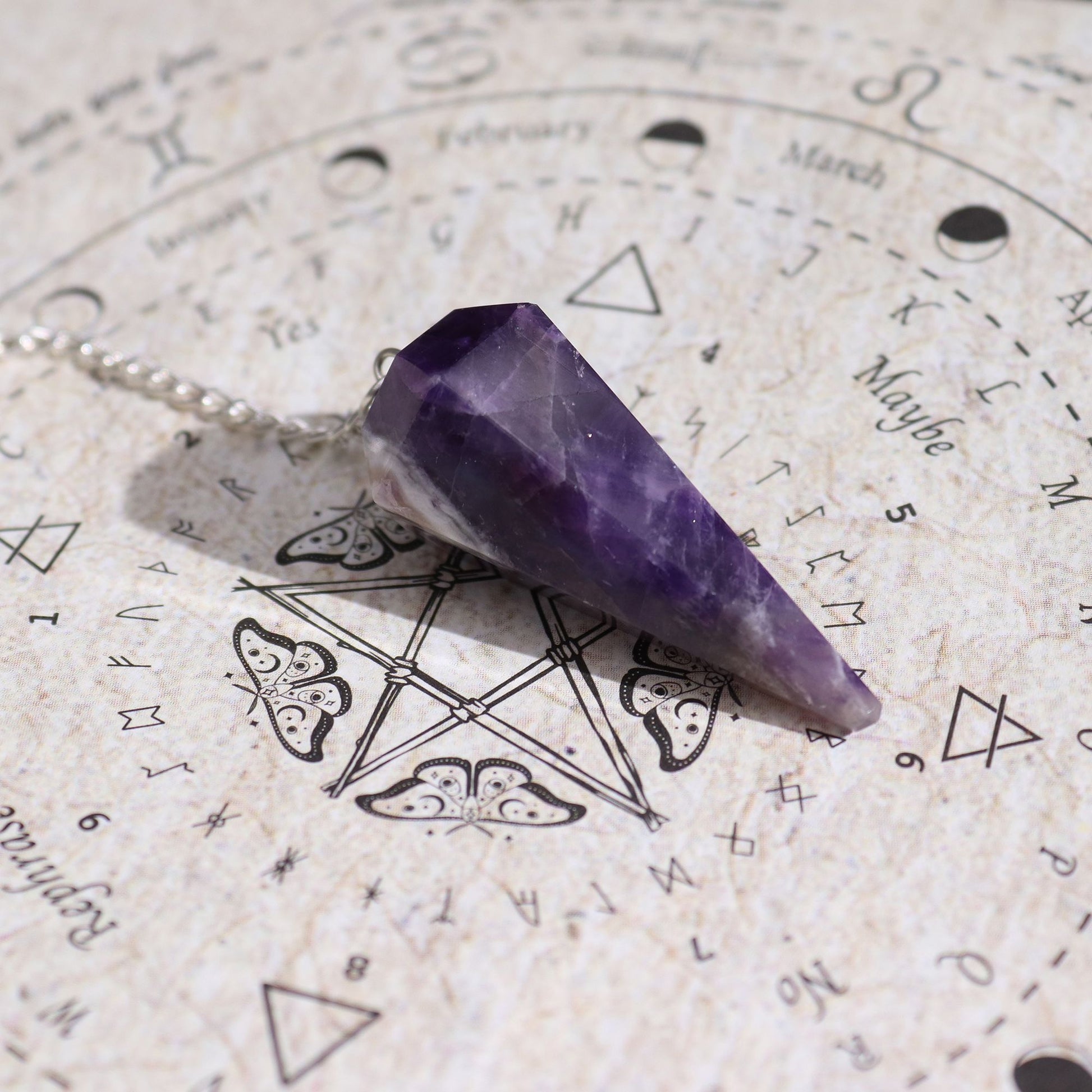 Amethyst pendulum pendant on a silver chain over an occult sigil background.